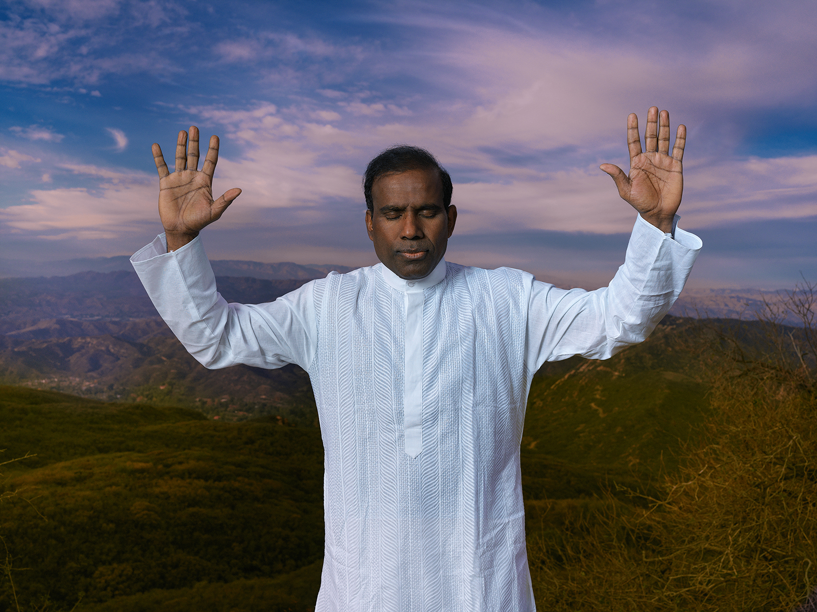 Dr. K.A. Paul with hands raised in worship over a mountain landscape